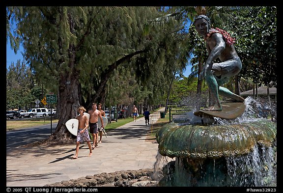 Young men carring surfboards next to statue of surfer, Kapiolani Park. Waikiki, Honolulu, Oahu island, Hawaii, USA