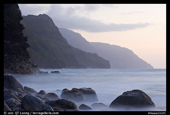 Boulders, surf, and Na Pali cliffs, sunset. Kauai island, Hawaii, USA