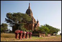 Five novices with red umbrellas walking below temple. Bagan, Myanmar