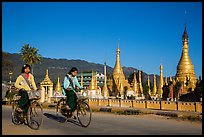 Schoolgirls riding bicycles past golden stupas. Pindaya, Myanmar ( color)