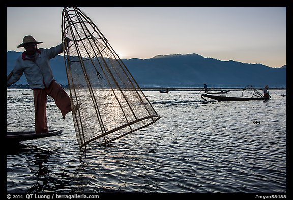 Intha fisherman standing on boat stern to lift net basket. Inle Lake, Myanmar (color)
