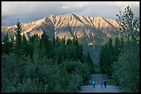 People walking on unpaved road, with last light on mountains. McCarthy, Alaska, USA (color)