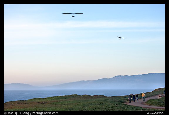 Hang gliders soaring above hikers, Fort Funston, late afternoon. San Francisco, California, USA