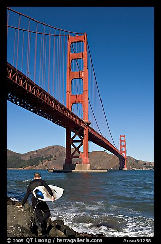 Surfer stepping on rocks and Golden Gate Bridge. San Francisco, California, USA (color)