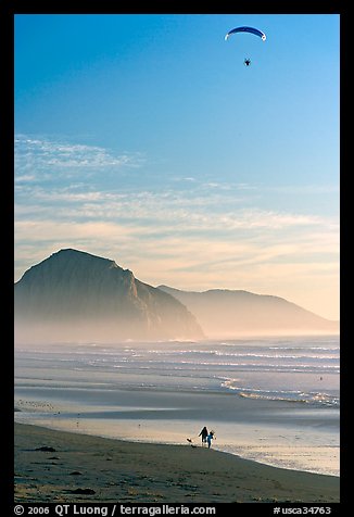 Motorized paraglider, women walking dog, and Morro Rock seen from Cayucos Beach. Morro Bay, USA (color)