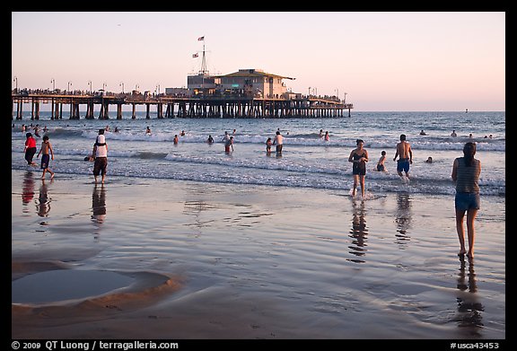 Beachgoers near Santa Monica Pier reflected in wet sand, sunset. Santa Monica, Los Angeles, California, USA