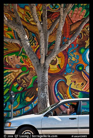 Man smoking in car, tree, and mural, Mission District. San Francisco, California, USA