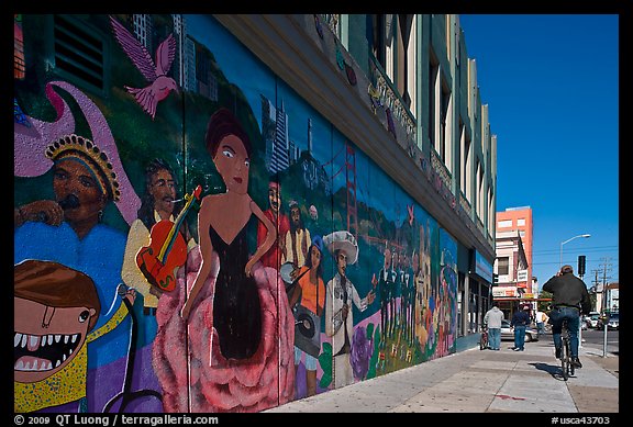 Man riding bicycle on sidewalk past mural, Mission District. San Francisco, California, USA (color)