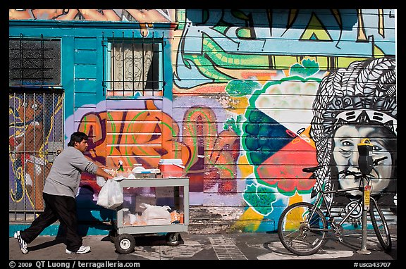 Man pushes vending cart pass mural and bicycle, Mission District. San Francisco, California, USA (color)