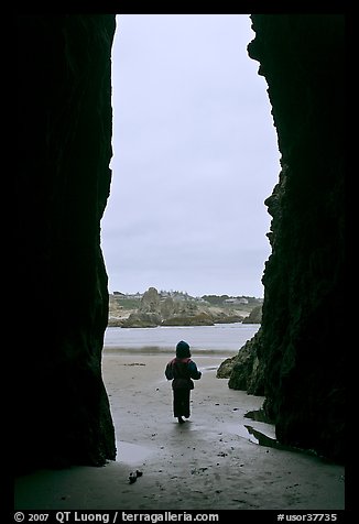 Infant standing at sea cave opening. Bandon, Oregon, USA