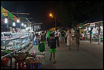 Shoppers walk past craft booth at night market. Phu Quoc Island, Vietnam