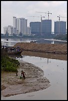 Man wading in mud, with background of towers in construction, Phu My Hung, district 7. Ho Chi Minh City, Vietnam