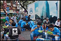Uniformed students eating breakfast in front of backdrop depicting high rise in construction. Ho Chi Minh City, Vietnam (color)