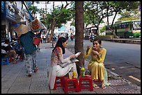 Women elegantly dressed in ao dai eating on the street. Ho Chi Minh City, Vietnam