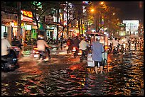 Traffic passes man pushing food cart on flooded street at night. Ho Chi Minh City, Vietnam