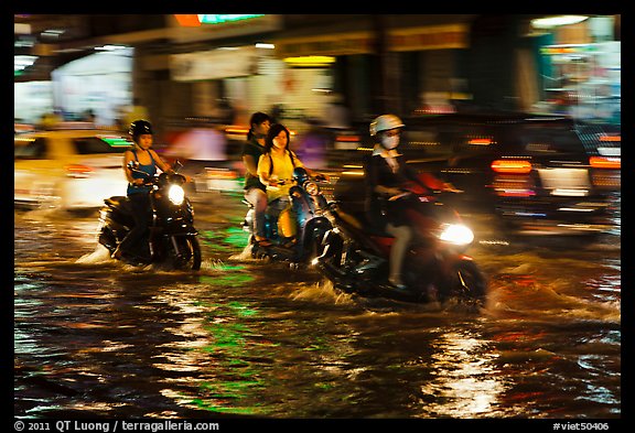 Women riding motorcyles at night in water. Ho Chi Minh City, Vietnam