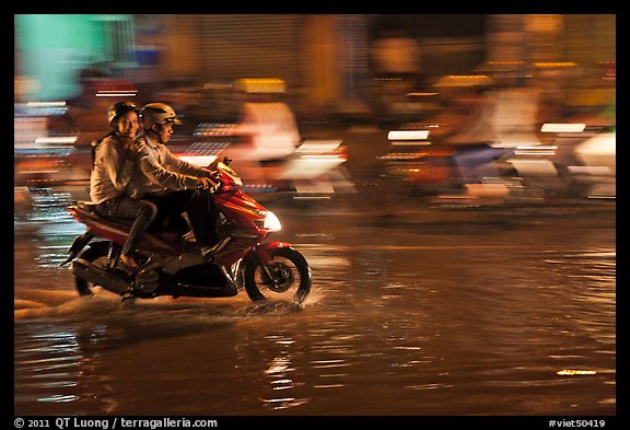 Couple sharing fast night ride on wet street. Ho Chi Minh City, Vietnam