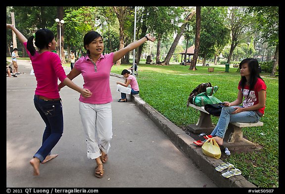 Young women dancing to sound of mobile phone, Tao Dan Park. Ho Chi Minh City, Vietnam (color)