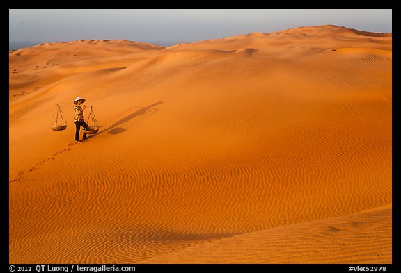 Red sand dunes and woman with carrying pole and baskets. Mui Ne, Vietnam