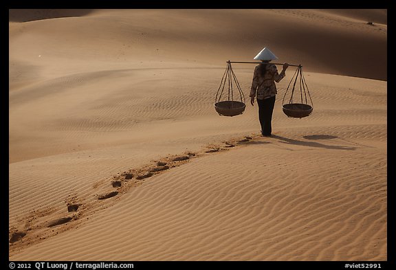 Woman walking on sand with two shoulder baskets. Mui Ne, Vietnam (color)