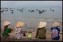 Four women in conical hats watch fishing activity from high above fishing village. Mui Ne, Vietnam ( color)