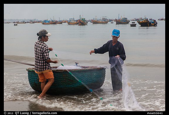 Man and woman gathering fishing net onto roundboat. Mui Ne, Vietnam