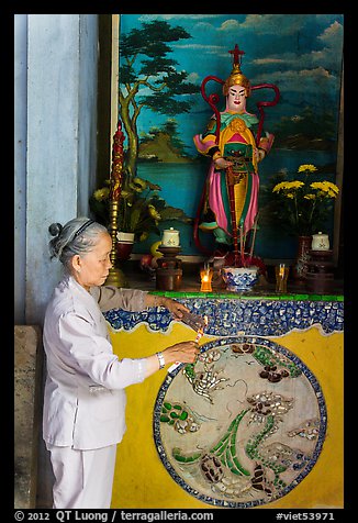 Woman lighting incense at side altar. Da Nang, Vietnam
