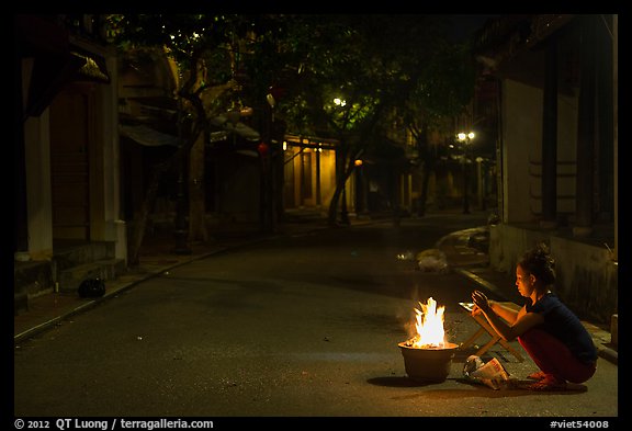 Woman burning paper on street at night. Hoi An, Vietnam (color)