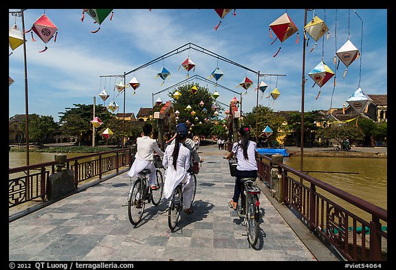 Girls on bicycle cross bridge festoned with lanterns. Hoi An, Vietnam (color)