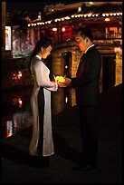 Couple holding candles in front of Japanese bridge at night. Hoi An, Vietnam (color)