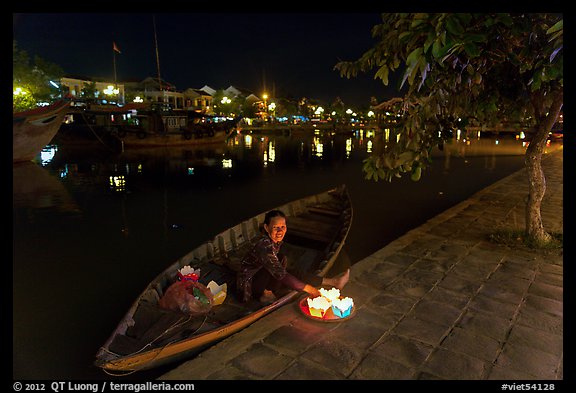 Woman sitting in rowboat selling candles on quay. Hoi An, Vietnam