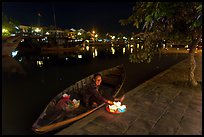 Woman sitting in rowboat selling candles on quay. Hoi An, Vietnam (color)