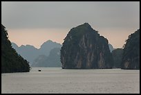 Fishing boat dwarfed by limestone islands. Halong Bay, Vietnam ( color)