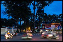 Blurred motorbikes at dusk and tall trees next to Van Hoa Park. Ho Chi Minh City, Vietnam