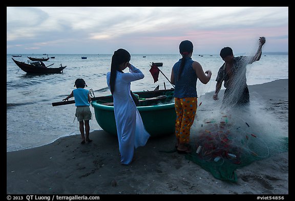 Fishermen folding net out of coracle boat as children watch. Mui Ne, Vietnam