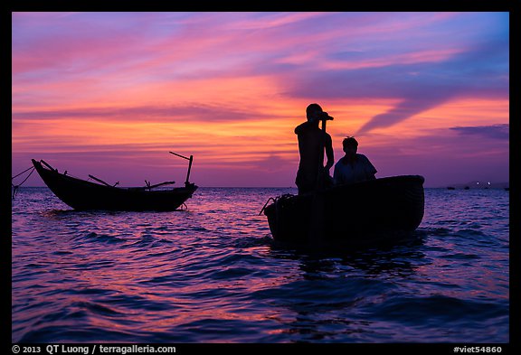 Men silhouetted paddling coracle boat at sunset. Mui Ne, Vietnam