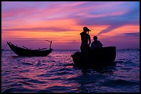 Men silhouetted paddling coracle boat at sunset. Mui Ne, Vietnam (color)