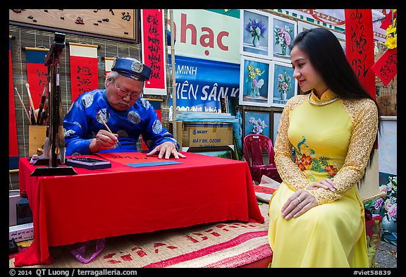 Caligrapher draws lunar new year greetings for beautiful woman in ao ai. Ho Chi Minh City, Vietnam (color)