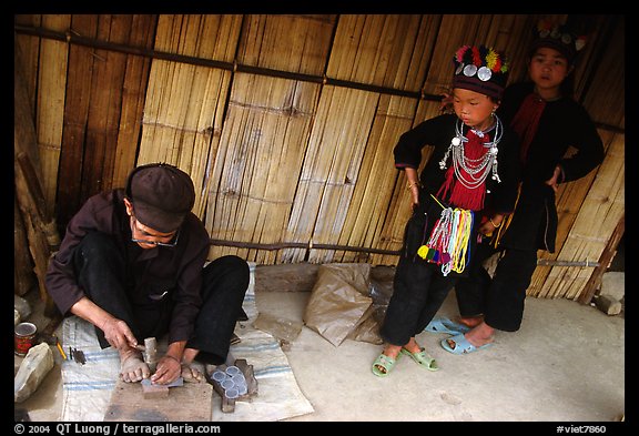 Black Dzao children look at a man  making the decorative coins used on their hats, between Tam Duong and Sapa. Northwest Vietnam (color)