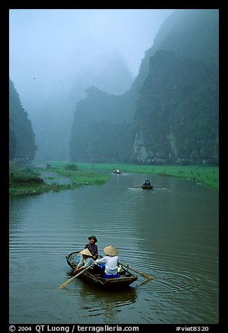 Villagers going by boat to their fields, amongst misty cliffs, Tam Coc. Ninh Binh,  Vietnam