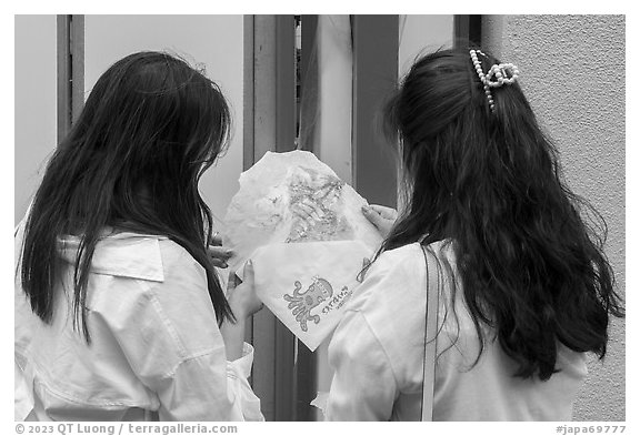 Women share tako senbei, snack made with roasted octopus pressed into a crispy sheet. Enoshima Island, Japan