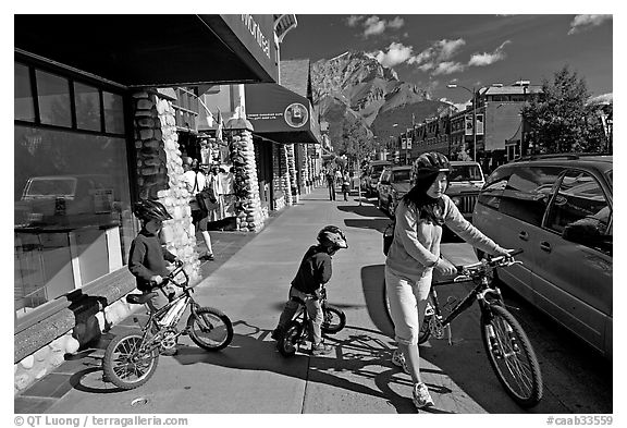 Woman and kids with mountain bikes on downtown Banff sidewalk. Banff National Park, Canadian Rockies, Alberta, Canada (black and white)