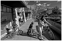 Woman and kids with mountain bikes on downtown Banff sidewalk. Banff National Park, Canadian Rockies, Alberta, Canada (black and white)