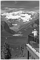 Man looking at Lake Louise through binoculars on observation platform. Banff National Park, Canadian Rockies, Alberta, Canada ( black and white)