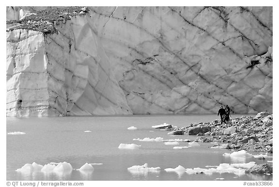 Hikers on the shore of Cavell Pond with high glacier wall behind. Jasper National Park, Canadian Rockies, Alberta, Canada