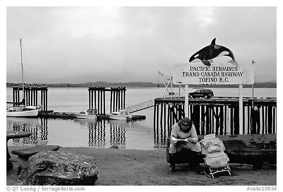 Backpacker sitting under the Transcanadian terminus sign, Tofino. Vancouver Island, British Columbia, Canada