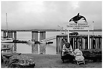 Backpacker sitting under the Transcanadian terminus sign, Tofino. Vancouver Island, British Columbia, Canada ( black and white)