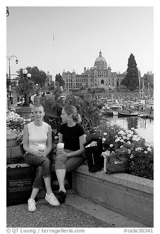 Women with shopping bags and coffee cups at the Inner Harbour, sunset. Victoria, British Columbia, Canada (black and white)