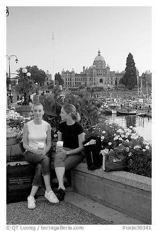 Women with shopping bags and coffee cups at the Inner Harbour, sunset. Victoria, British Columbia, Canada