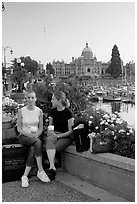 Women with shopping bags and coffee cups at the Inner Harbour, sunset. Victoria, British Columbia, Canada (black and white)